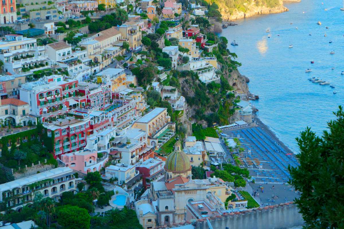 Dettaglio della cupola maiolicata della Chiesa di Santa Maria Assunta, inquadrata dal basso, con scorcio di cielo azzurro e tipici vicoli di Positano
