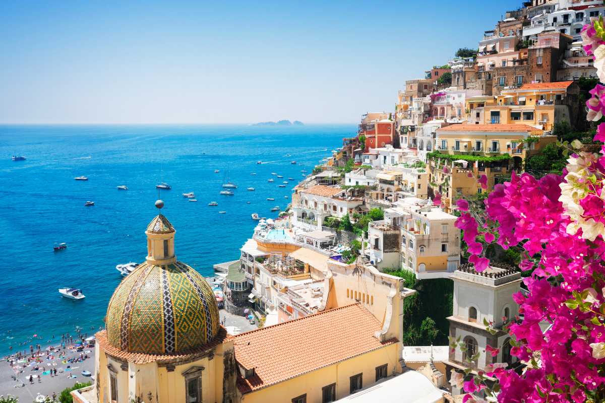Panorama dall’alto di Positano al tramonto, con case color pastello abbarbicate sulla scogliera, barche nel mare e una sensazione di estate italiana