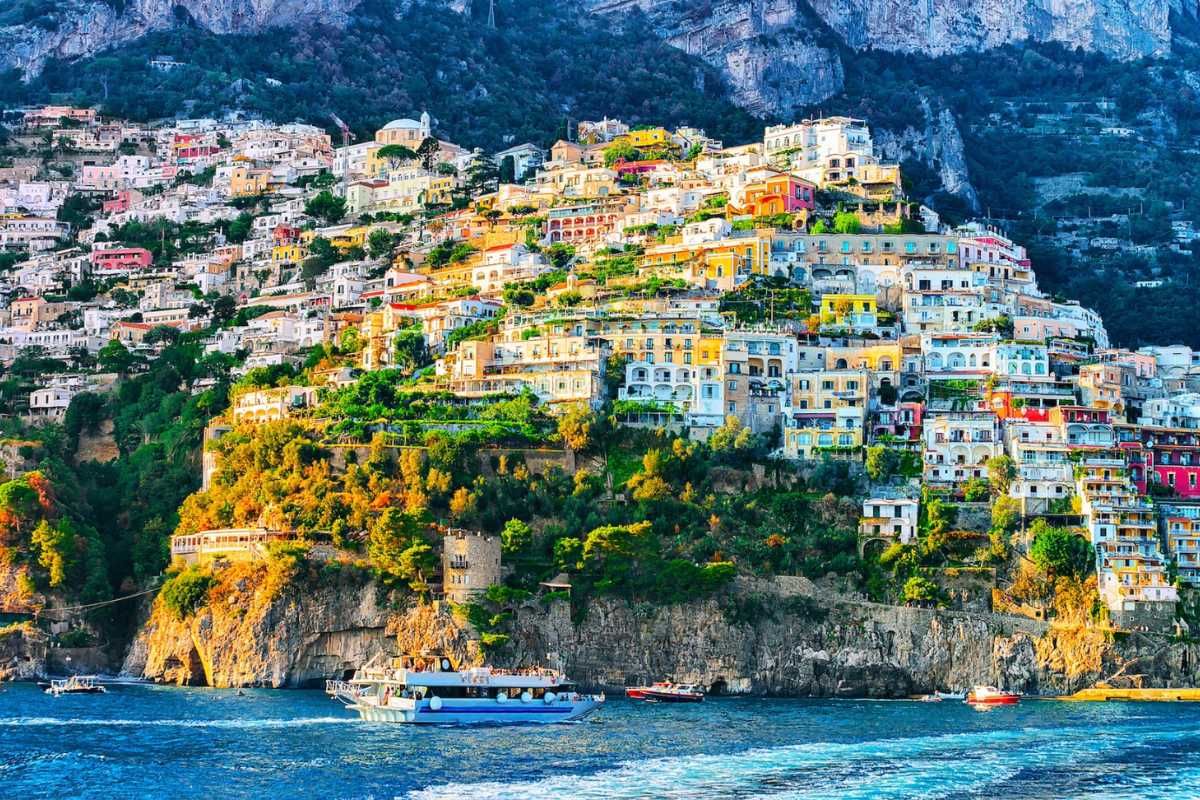 Turisti che percorrono un sentiero panoramico sopra Positano, vista sulle torri saracene, vegetazione mediterranea e mare cristallino