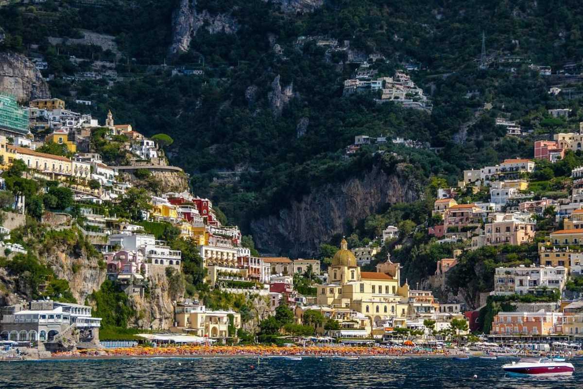 Laboratorio di ceramica con bambini sorridenti, tavolo colorato, artigiani locali che insegnano, dettagli di Positano sullo sfondo